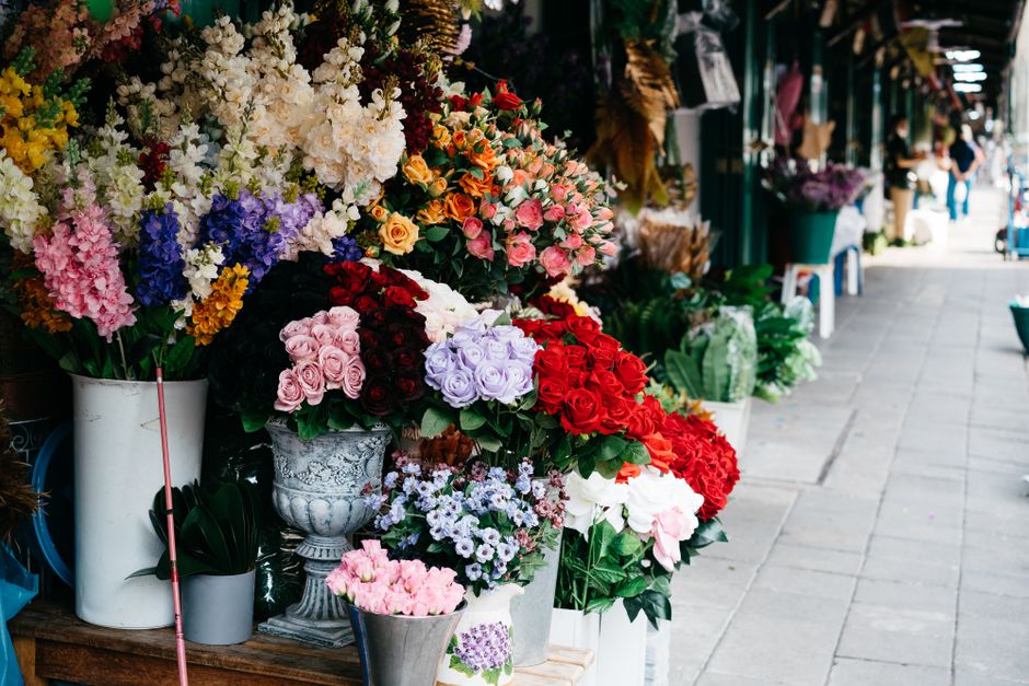 A vibrant display of fresh floral arrangements at a flower market, featuring a variety of roses, including pink, red, white, and lavender, alongside fragrant lilies and other colorful blossoms. The fl